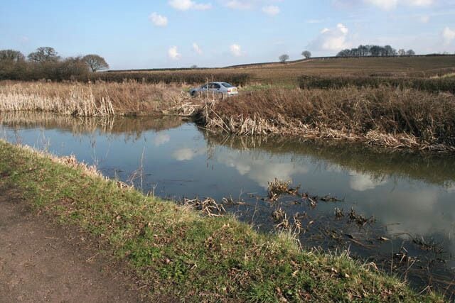 By the Nottingham Canal Cossall Road and the canal run side by side through most of their legth in this square. Here the canal and road cross a stream which is culverted under the waterway and road. Just in front of the car you can see an overflow outfall which feeds into this stream. The canal follows the 50m contour along this stretch and the trees in the distance are at 85 metres above sea level.