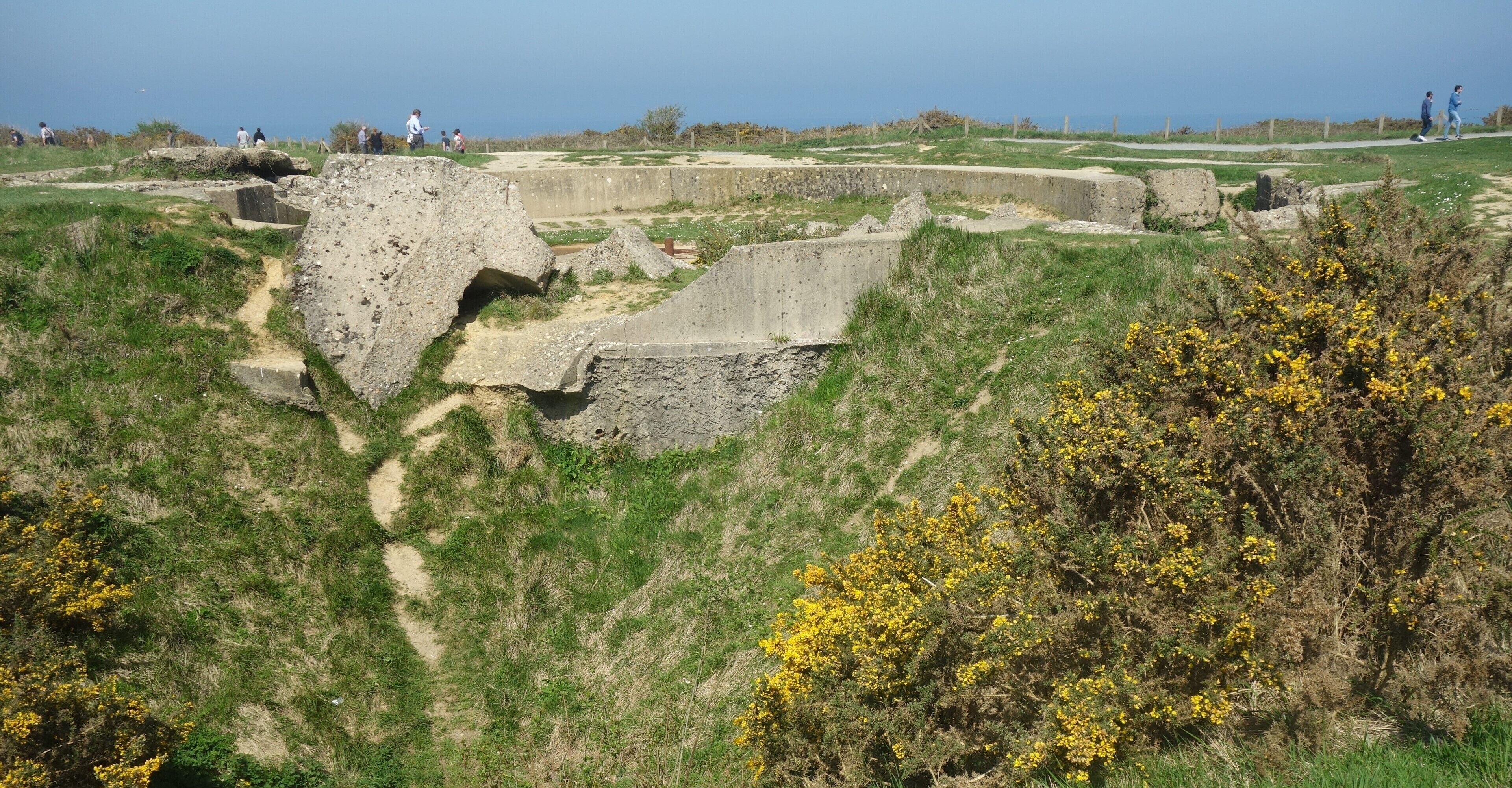 Ancient ruins with stone walls and pathways on a grassy hillside.