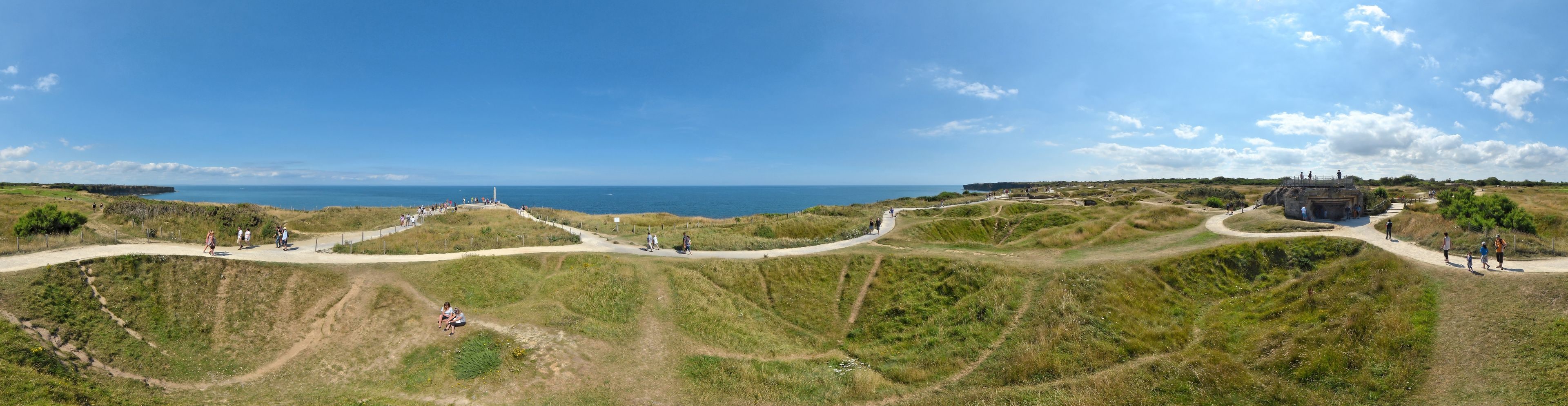 Un paysage côtier avec des dunes herbeuses, un ciel dégagé et une vue lointaine sur la mer.