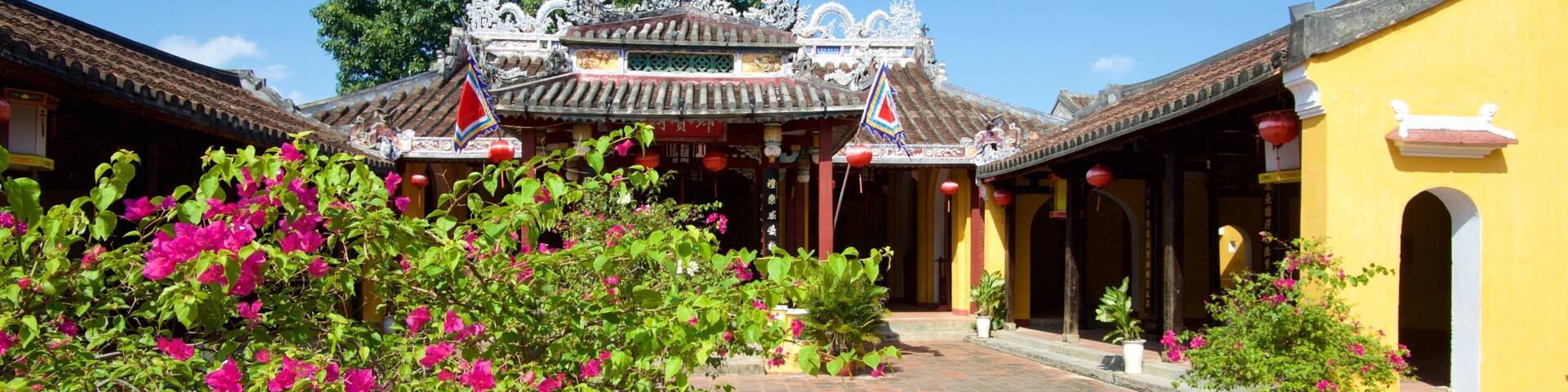 Un patio tradicional con arquitectura ornamentada, vibrantes flores de buganvilla y un cielo azul despejado.