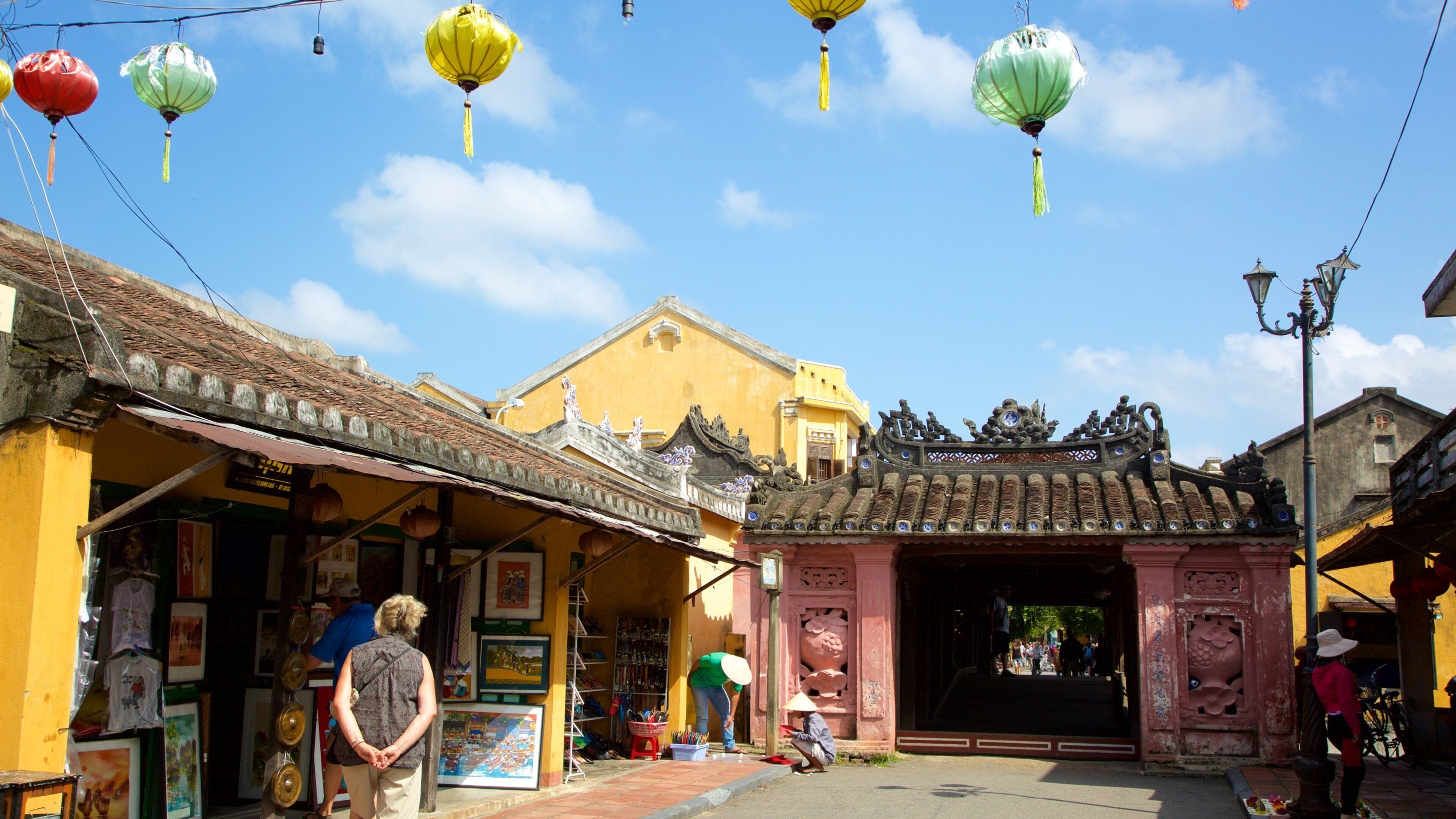 A traditional street with colorful lanterns, a yellow building, and a pink gate.