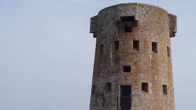 Uma torre de pedra circular com várias janelas e uma escadaria que leva a uma porta.