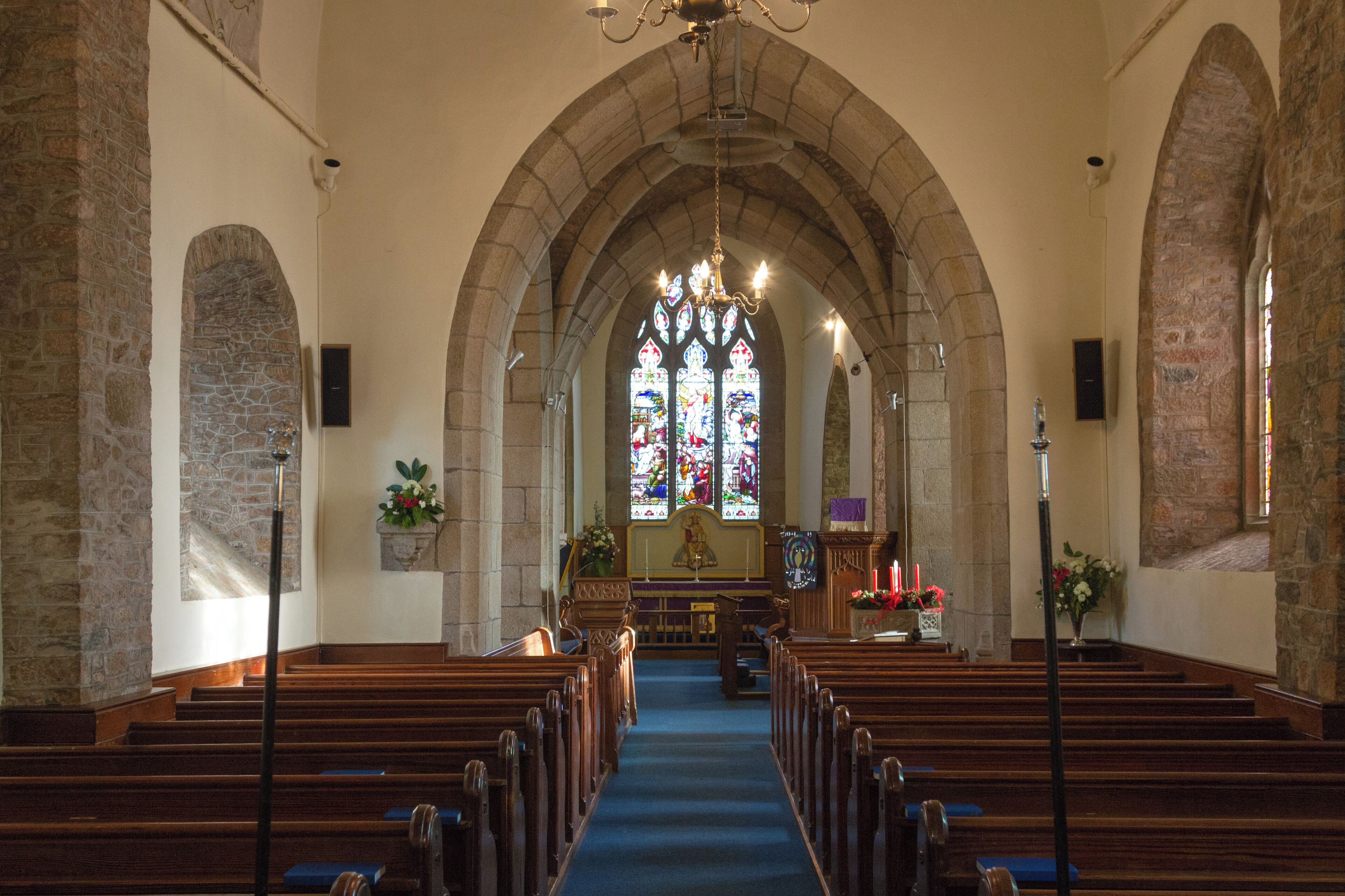 An interior of a church with wooden pews, a blue carpet, and a stained glass window.