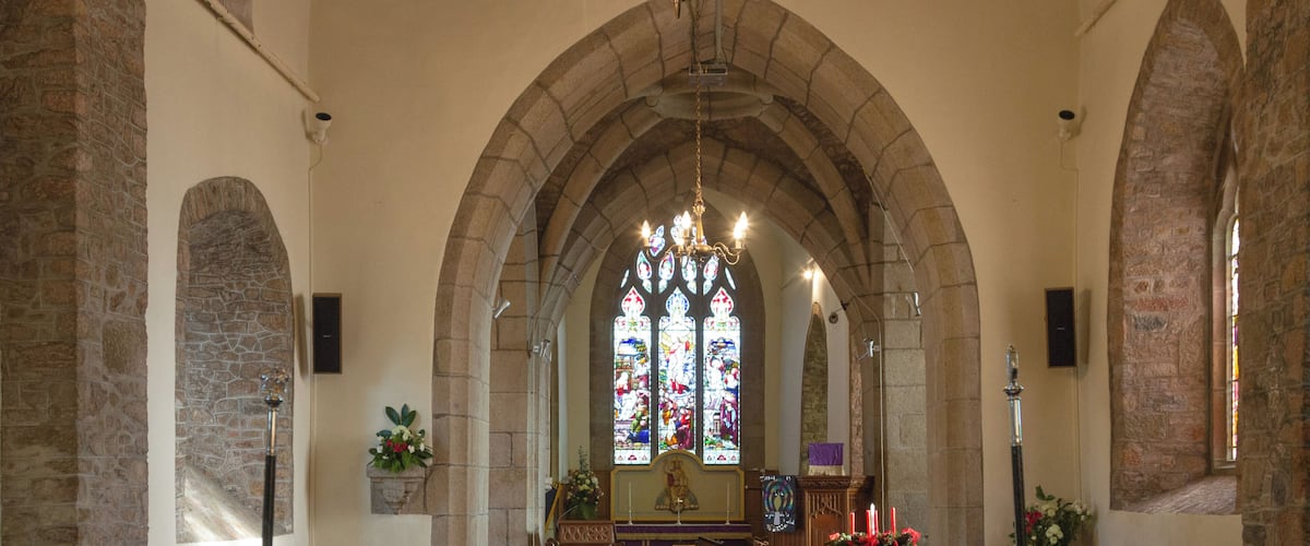 An interior of a church with wooden pews, a blue carpet, and a stained glass window.