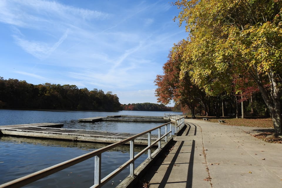 A lakeside walkway with wooden docks and autumn-colored trees.
