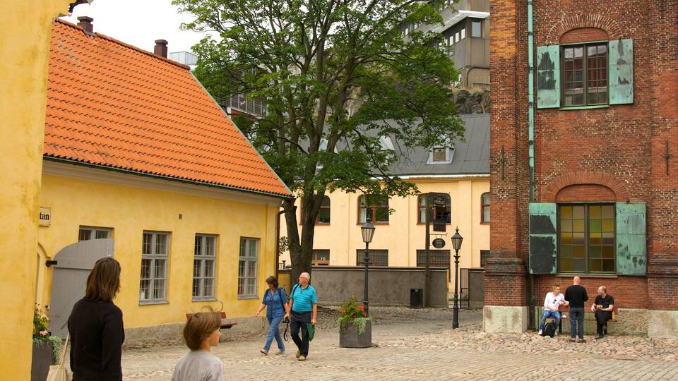 A cobblestone street with yellow and red buildings, a tree, and people walking.