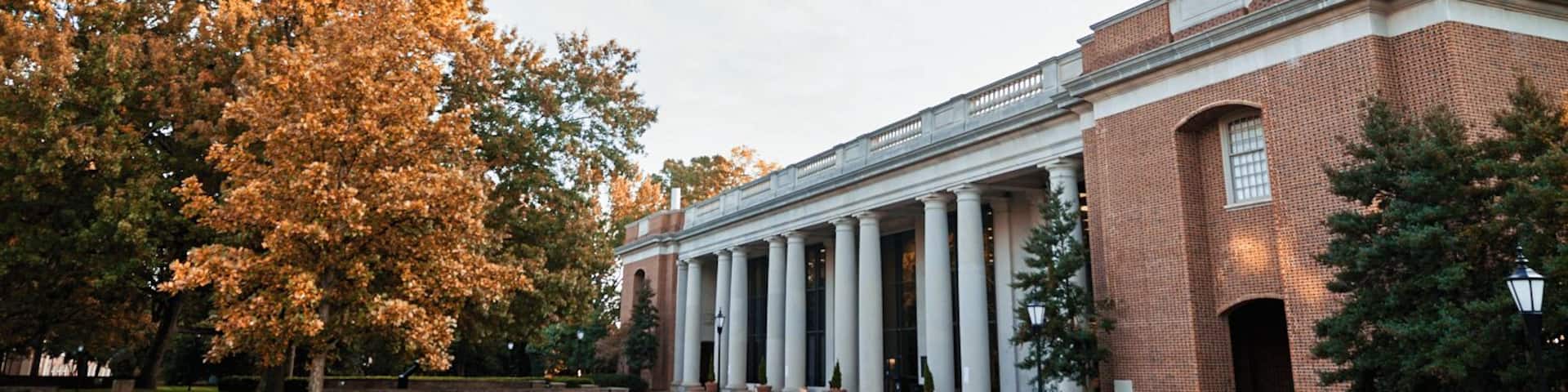 A large brick building with a portico and columns, surrounded by trees and a grassy area.