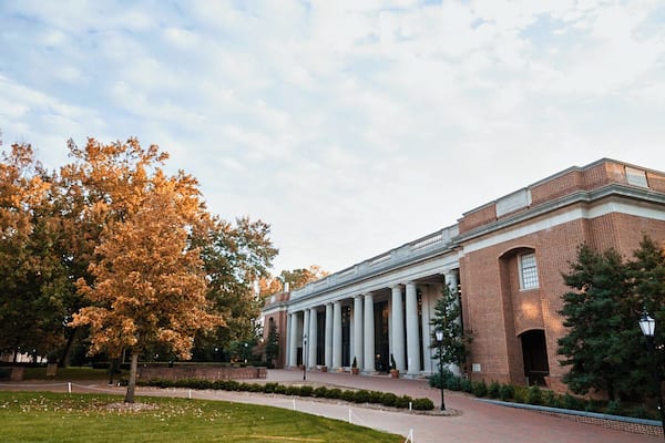 A large brick building with a portico and columns, surrounded by trees and a grassy area.