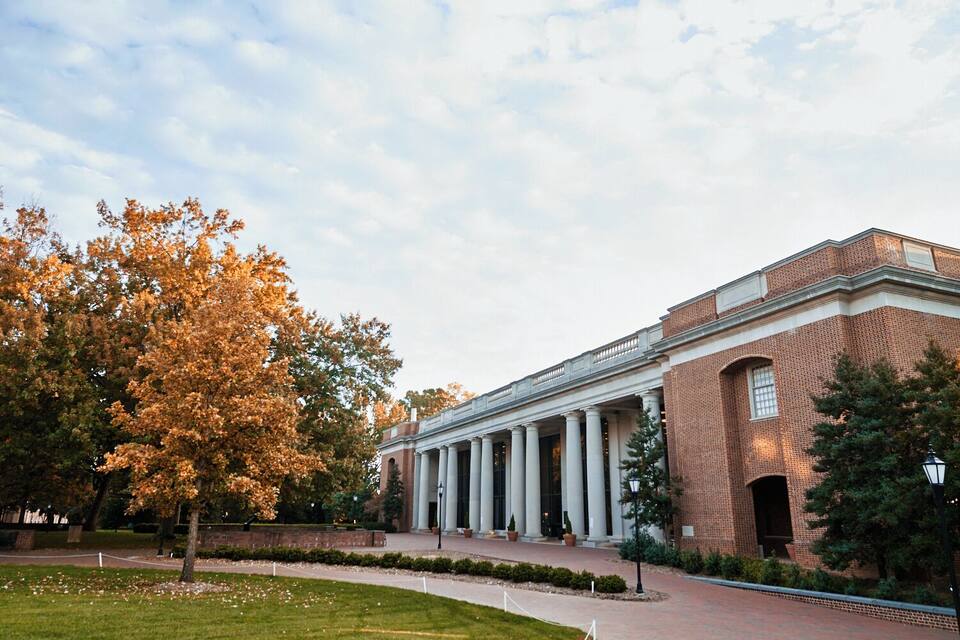 A large brick building with a portico and columns, surrounded by trees and a grassy area.