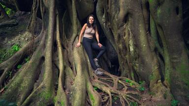 Young woman posing on a giant root tree in the tropical forest. Young woman in green wet forest on sunny day. Sustainable tourism concept. Amatlán, Mexico.
