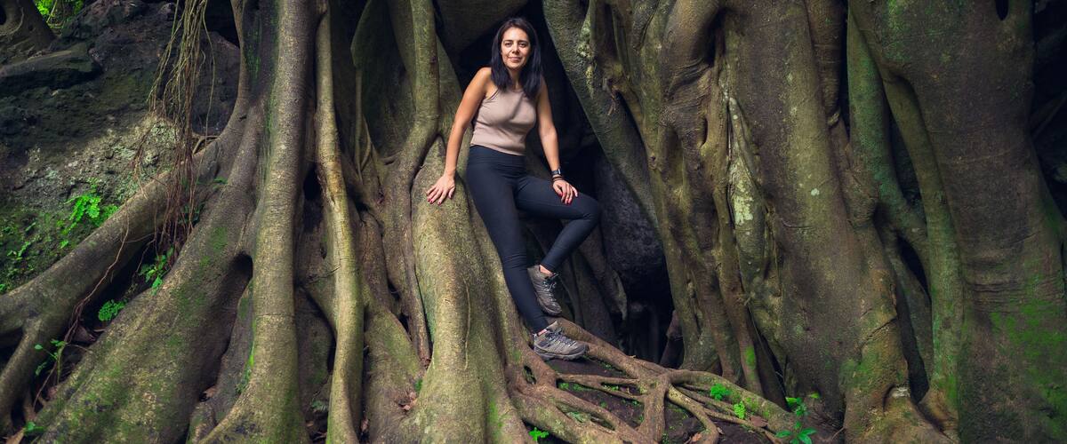 A person sitting among large tree roots in a forest.
