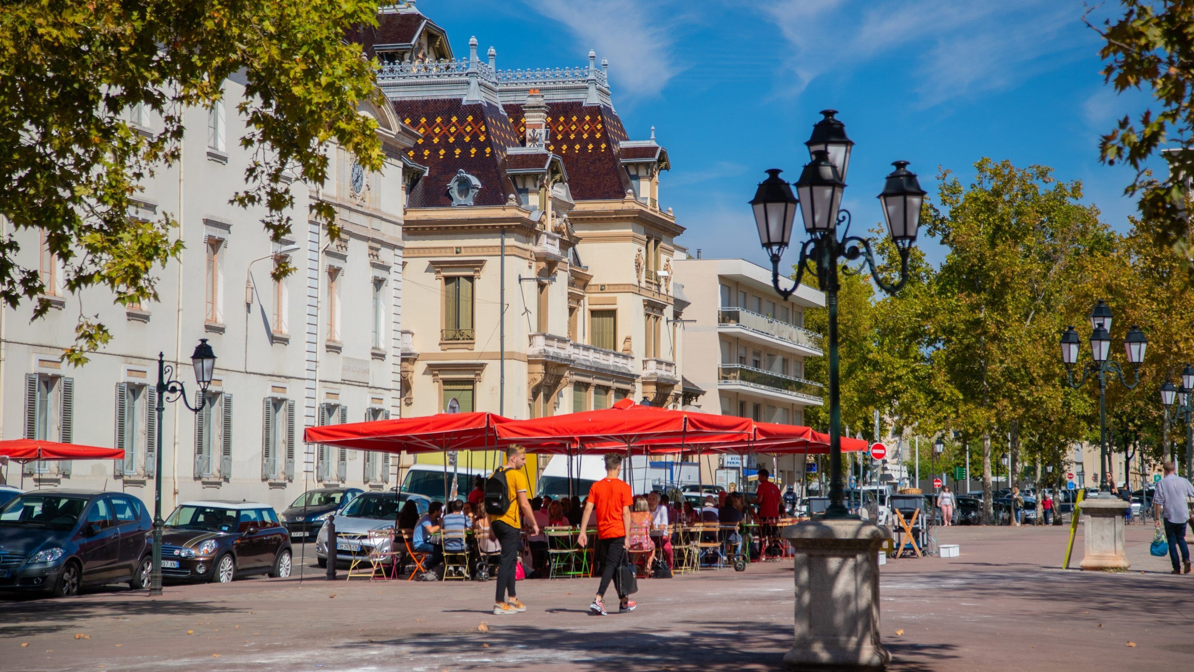 Une rue bordée de parasols rouges, de voitures garées et de bâtiments historiques.