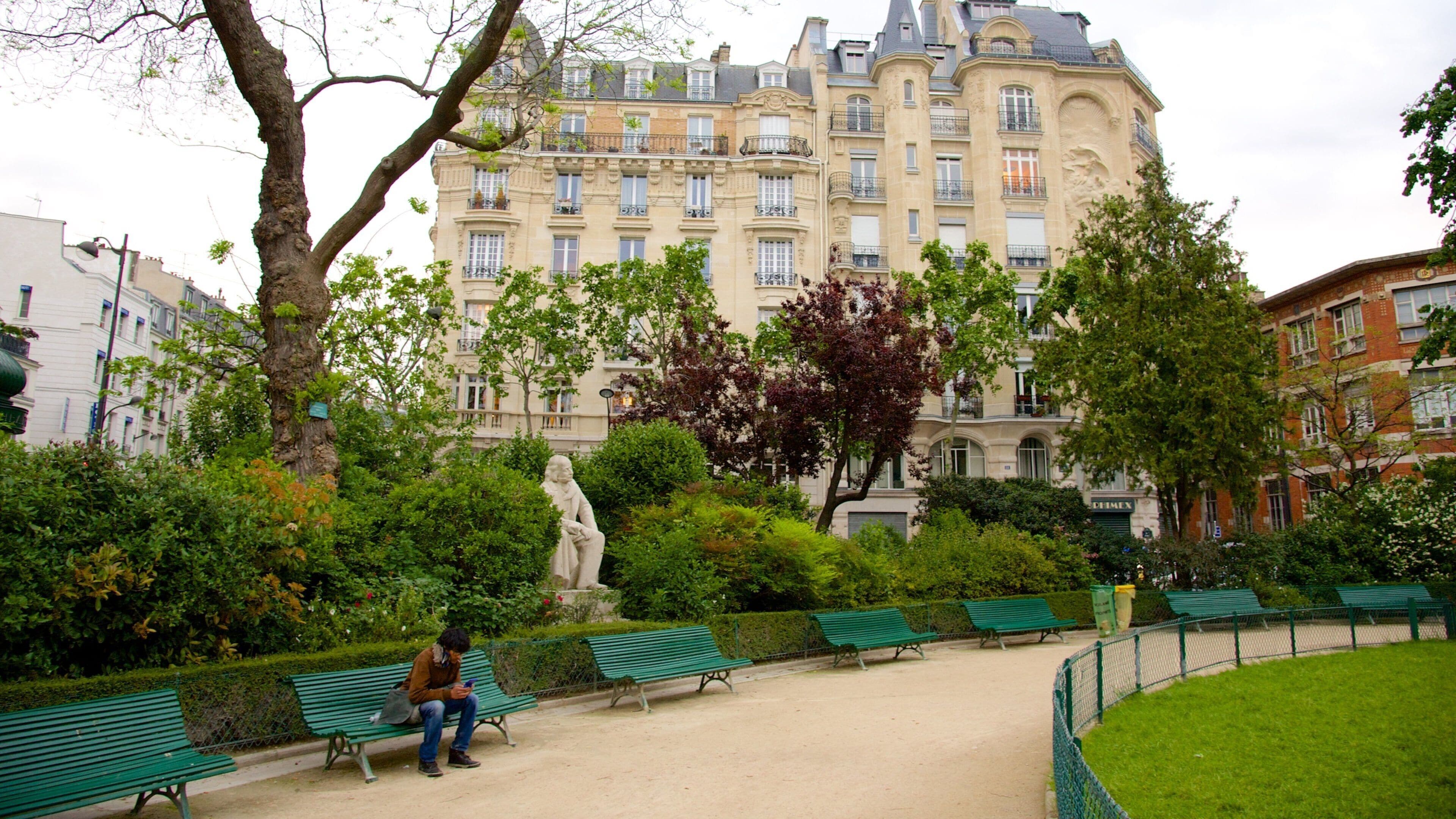 Um parque com bancos verdes, uma estátua e um edifício grande ao fundo.