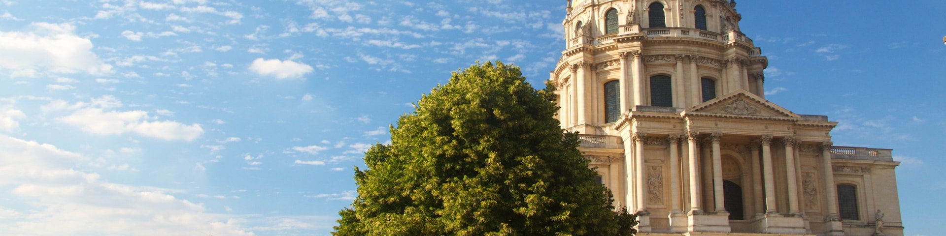A grand neoclassical building with a large dome and columns, surrounded by well-manicured gardens and a clear blue sky.