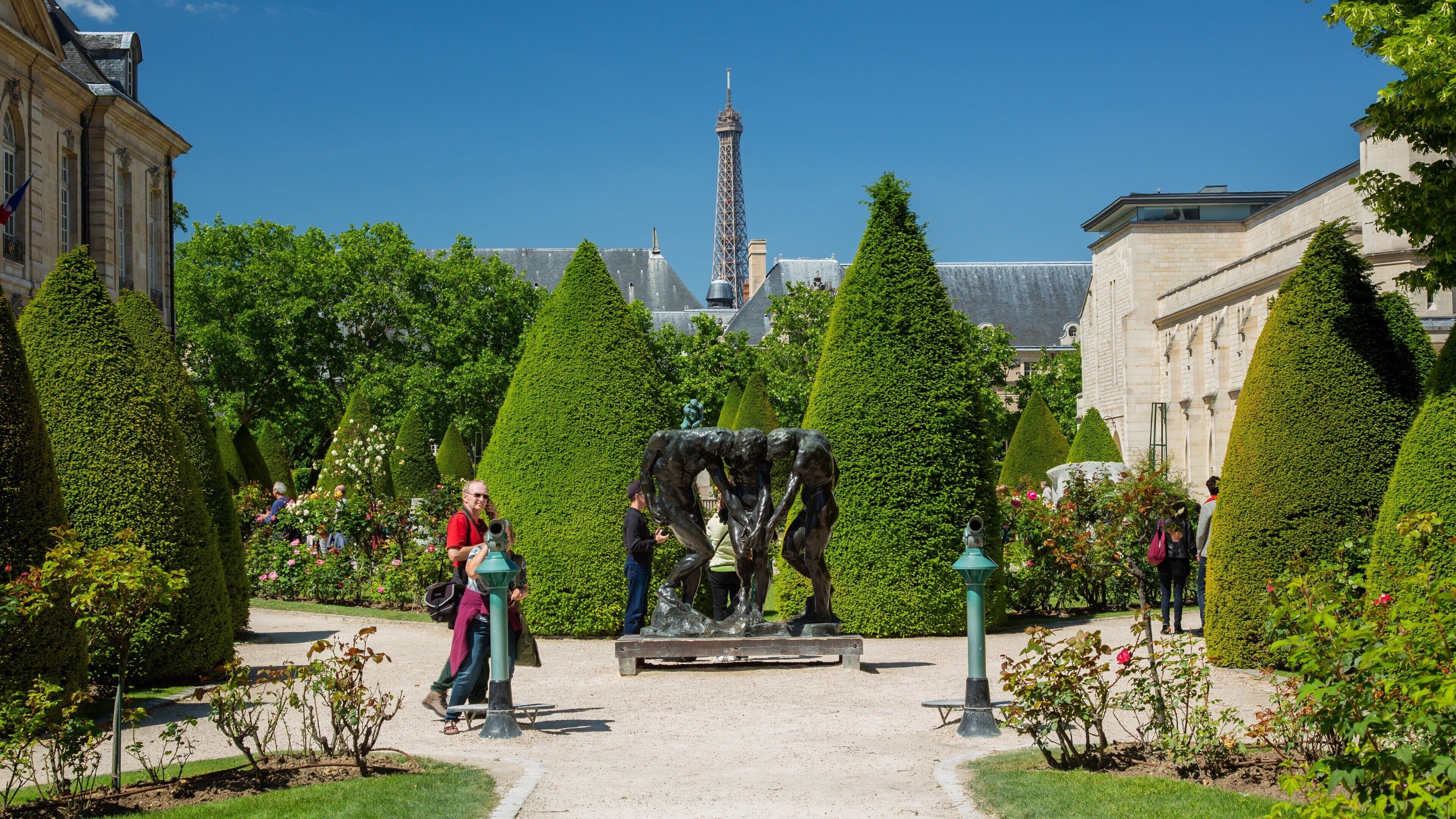 Um jardim com esculturas de topiaria, uma fonte e a Torre Eiffel ao fundo.