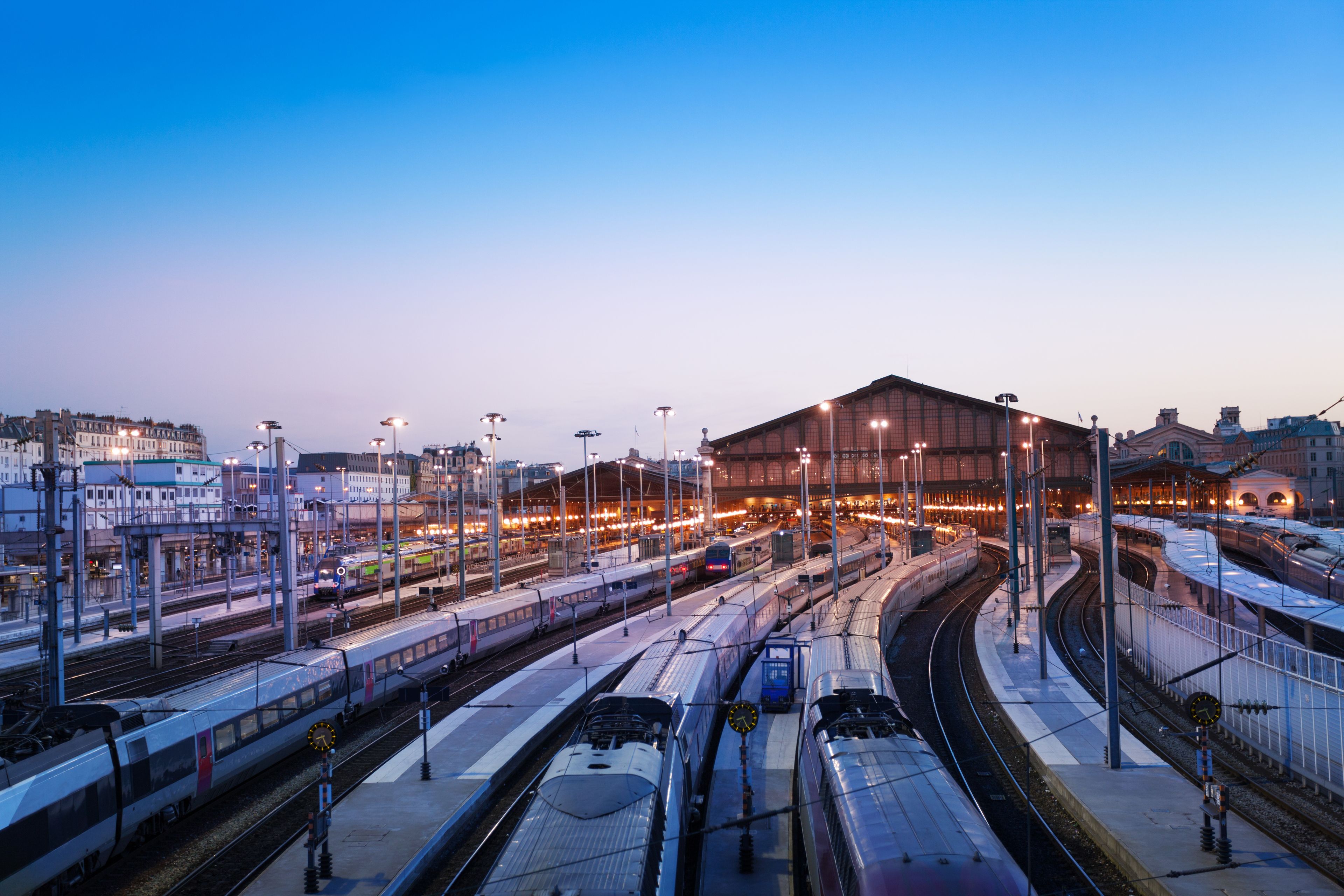 Una vivace stazione ferroviaria con diverse banchine e treni, circondata da edifici e lampioni.
