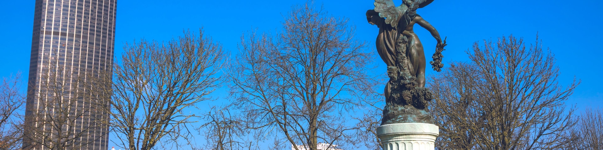Uma estátua de anjo com asas abertas, um edifício moderno alto e um cemitério com lápides.