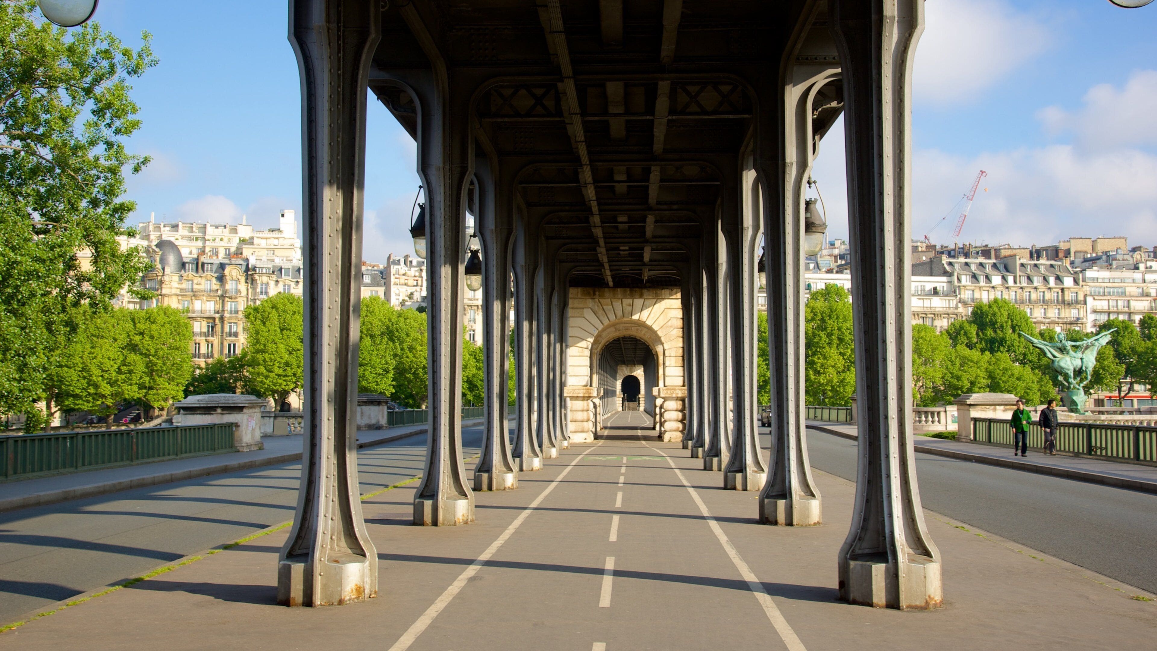 Uma ponte para pedestres com colunas de metal ornamentadas e uma passagem em arco.