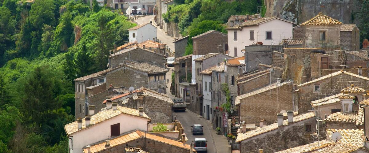A hillside village with terracotta-roofed buildings, a narrow street, and lush greenery.