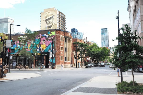 A street with a colorful mural on a building, a crosswalk, and cars on the road.