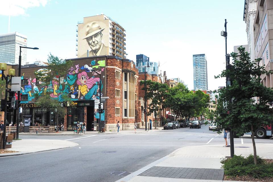 Una calle con un mural colorido en un edificio, un paso de peatones y coches en la vía.
