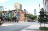 A street with a colorful mural on a building, a crosswalk, and cars on the road.