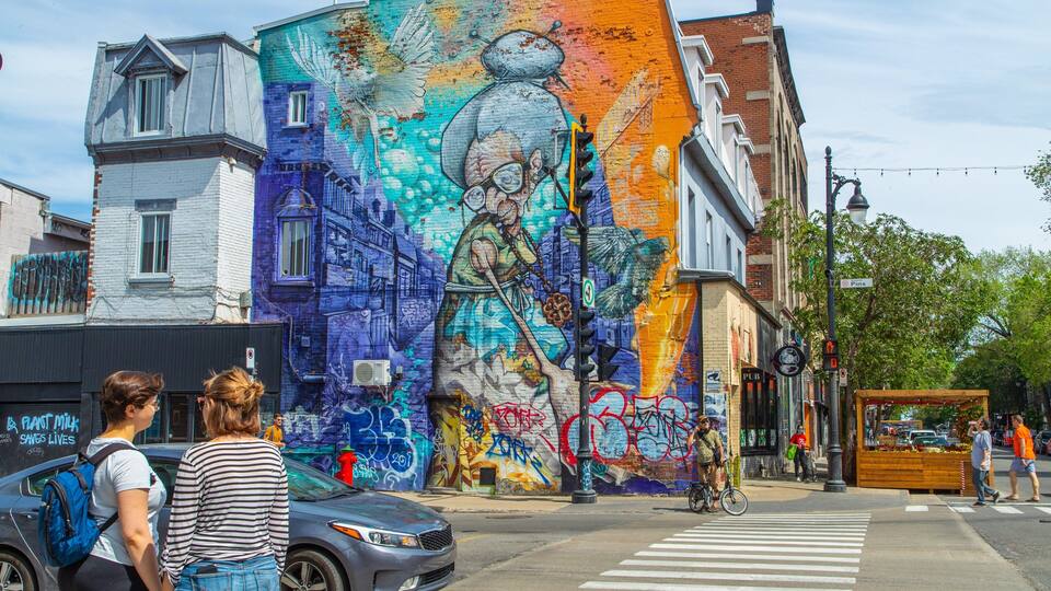 A vibrant mural on a building, a crosswalk, and a street with pedestrians and cyclists.