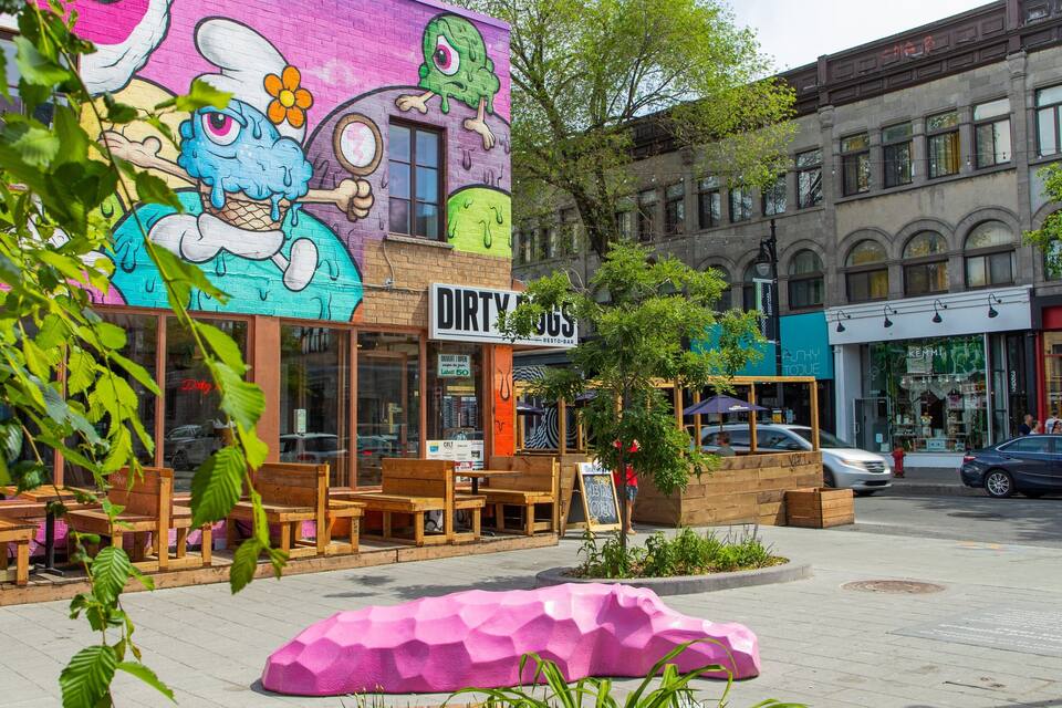 A colorful mural on a building, outdoor seating, and a pink sculpture.