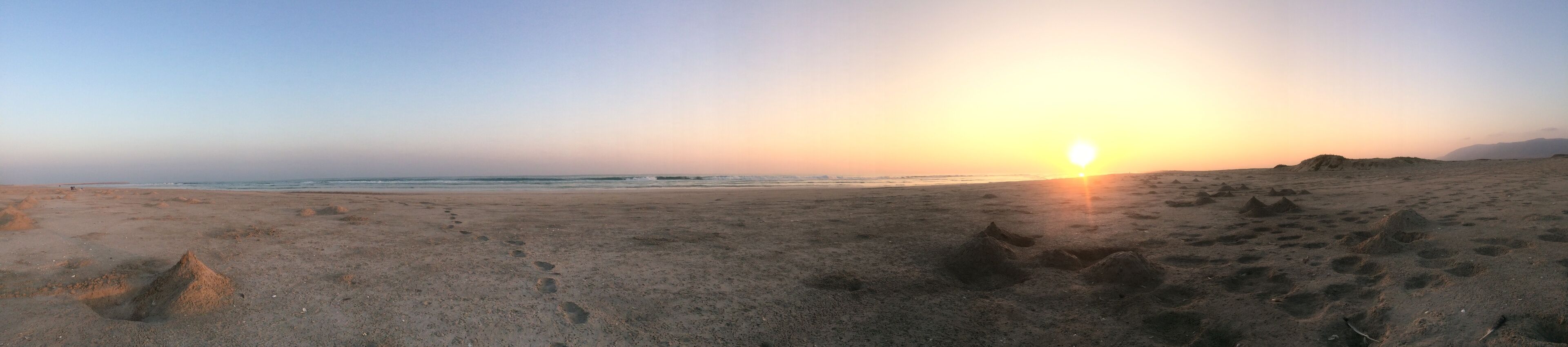A beach at sunset with footprints and sand mounds.