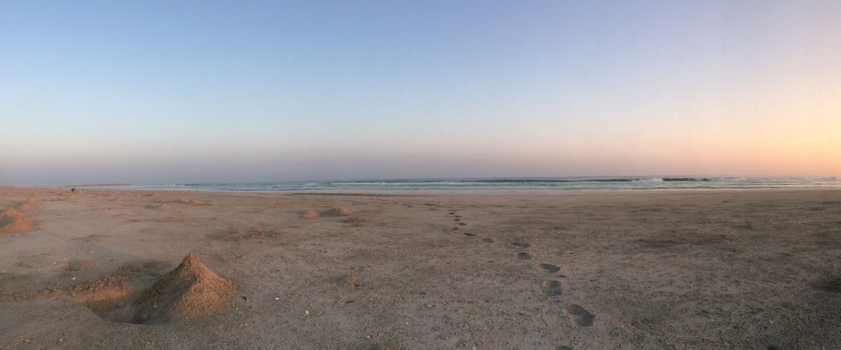 A beach at sunset with footprints and sand mounds.