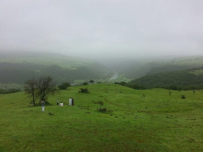A foggy valley with green hills and a few people walking.