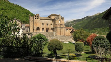 Un edificio histórico de piedra con ventanas de arco y un campanario, rodeado de exuberantes colinas y árboles verdes.