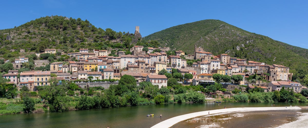 A hillside town with colorful buildings, a river, and a mountain in the background.