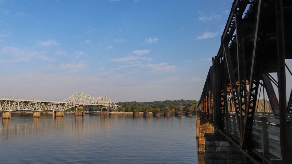 A steel bridge over calm water with a clear sky.