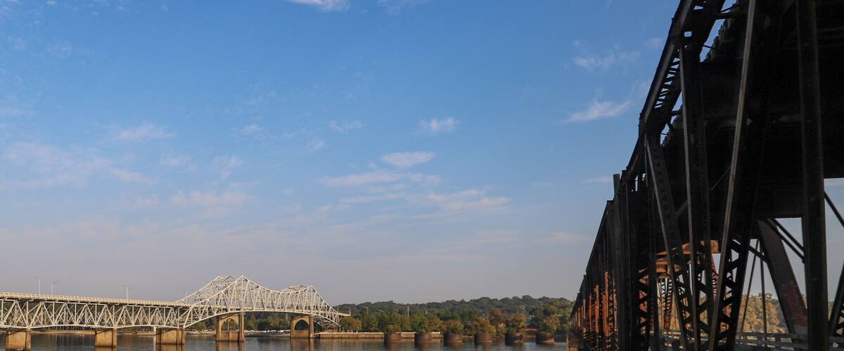 A steel bridge over calm water with a clear sky.