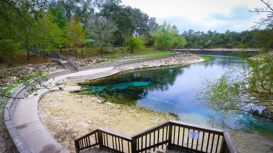 A clear, shallow water body with a wooden deck and stairs leading down to the water's edge.
