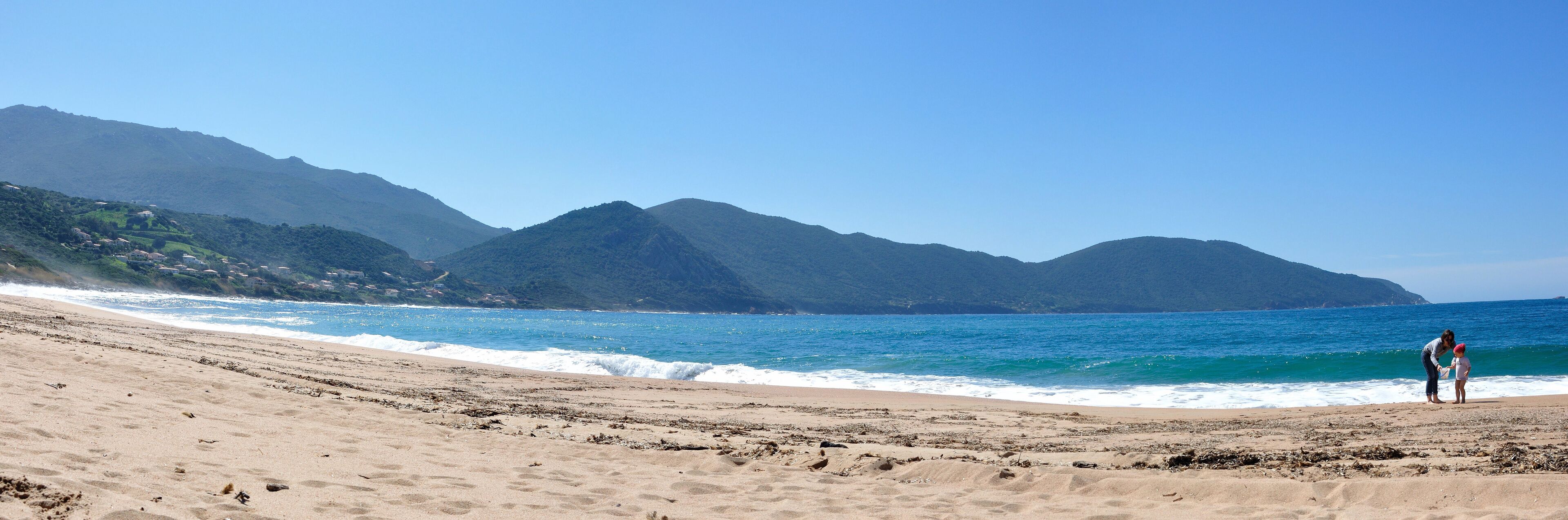 A beach with waves, mountains, and a clear sky.