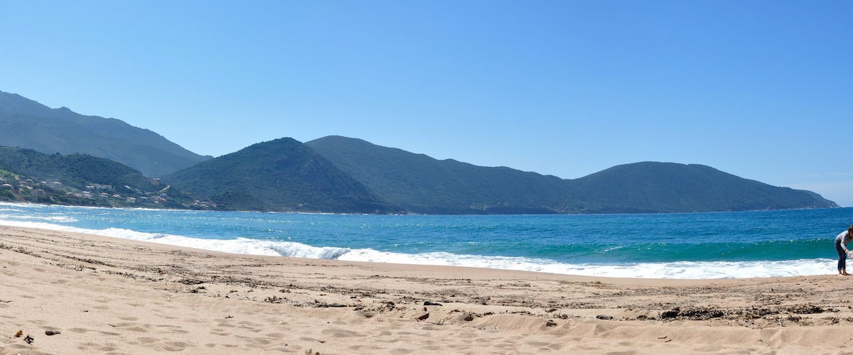 A beach with waves, mountains, and a clear sky.