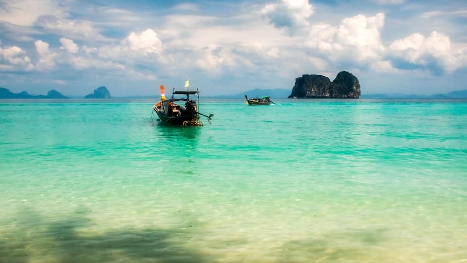 A boat on turquoise water with a rocky island in the background.