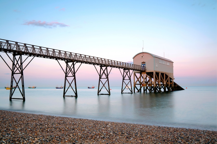A pebbled beach with a wooden pier extending into calm waters.