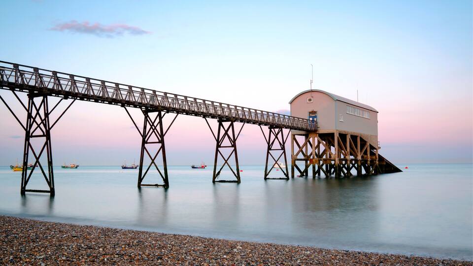 A pebbled beach with a wooden pier extending into calm waters.