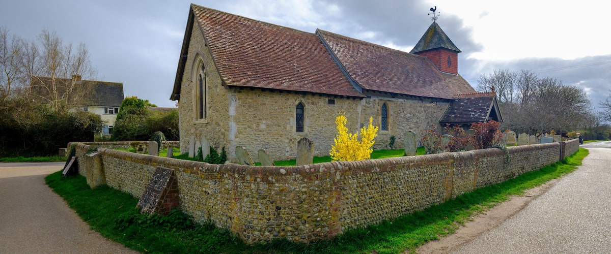 A stone church with a red-tiled roof, a weather vane, and a cemetery with headstones.