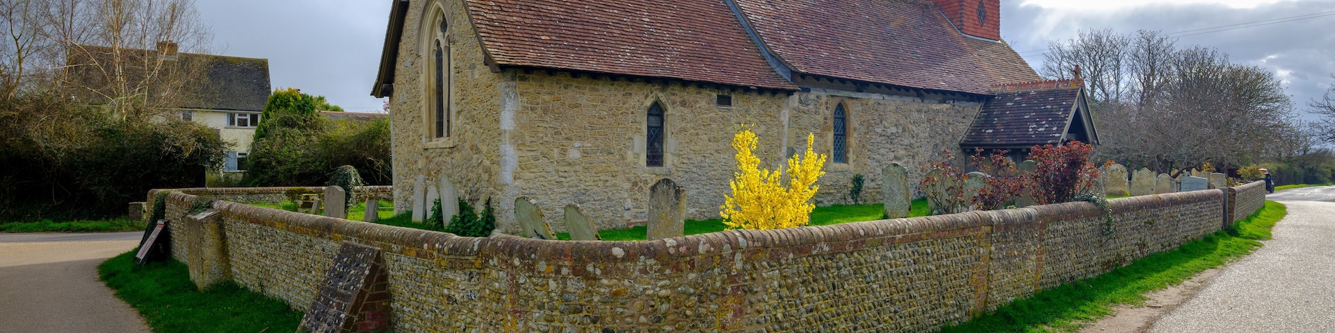 A stone church with a red-tiled roof, a weather vane, and a cemetery with headstones.