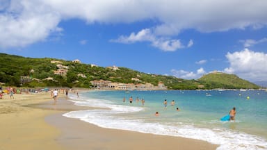 A beach with people swimming and walking along the shore, surrounded by buildings and hills.