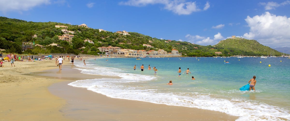 A beach with people swimming and walking along the shore, surrounded by buildings and hills.