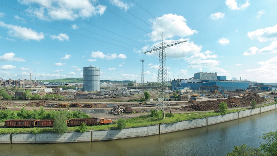A river with industrial facilities, including a large blue building and a water tower.