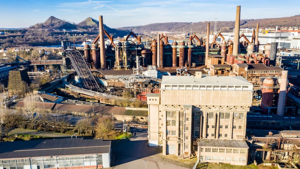 An industrial complex with multiple tall chimneys, a large building, and a conveyor belt system.