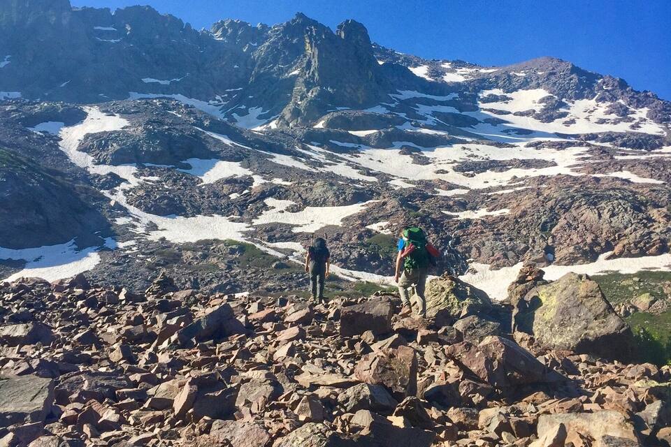 Een rotsachtig berglandschap met wandelaars en sneeuwvlekken.