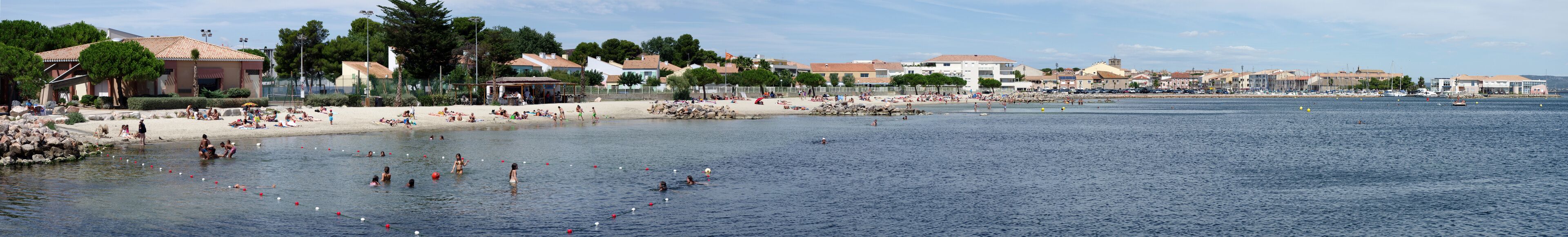 A coastal town with a sandy beach, clear blue water, and a variety of buildings along the shore.