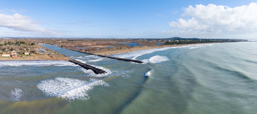 Un paisaje costero con un río, un espigón y una costa lejana con edificios.